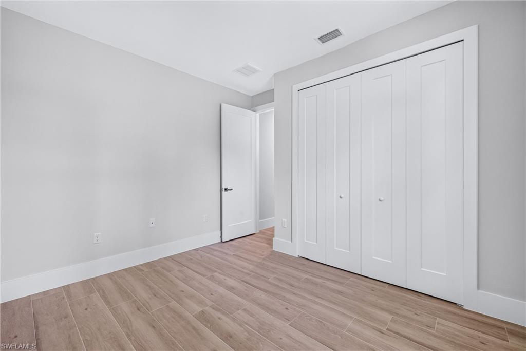 Spacious interior room featuring wood-finish flooring, light gray wall paint, white trim, and white bi-fold closet doors