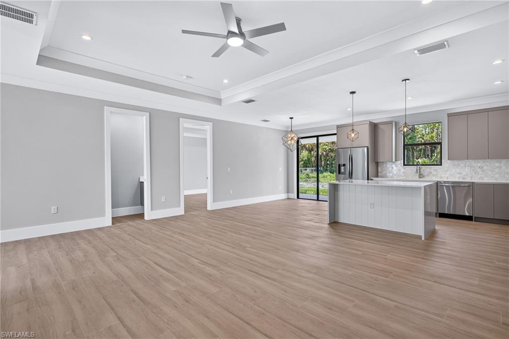 Expansive open concept living area featuring wood-finish flooring, a kitchen island with pendant lighting, stainless steel appliances, and a tray ceiling with recessed lighting