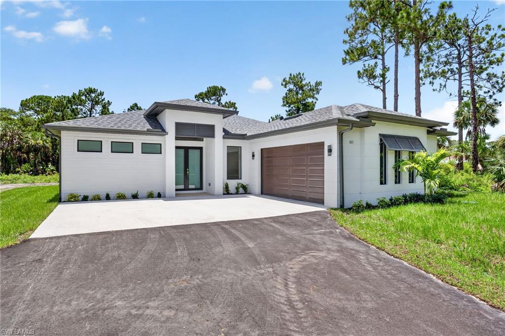 Contemporary single-story residence featuring a white exterior with dark trim accents, a two-car garage with a wood-finish door, a dark asphalt driveway, and a concrete paver walkway