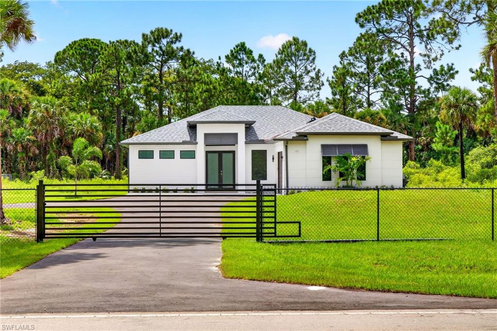 Contemporary white exterior with a gray shingle roof, black entry gate, and asphalt driveway