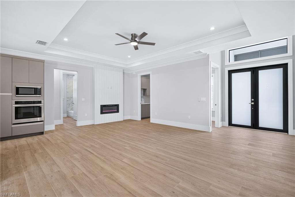 Spacious open-concept living area featuring wood-finish flooring, a contemporary electric fireplace with vertical shiplap detailing, and a tray ceiling with recessed lighting and a ceiling fan