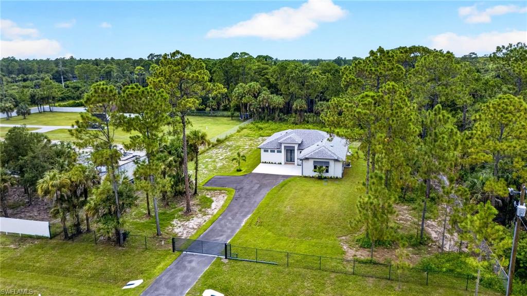 Gated entry with a paved driveway, lush green lawn, and surrounding mature trees