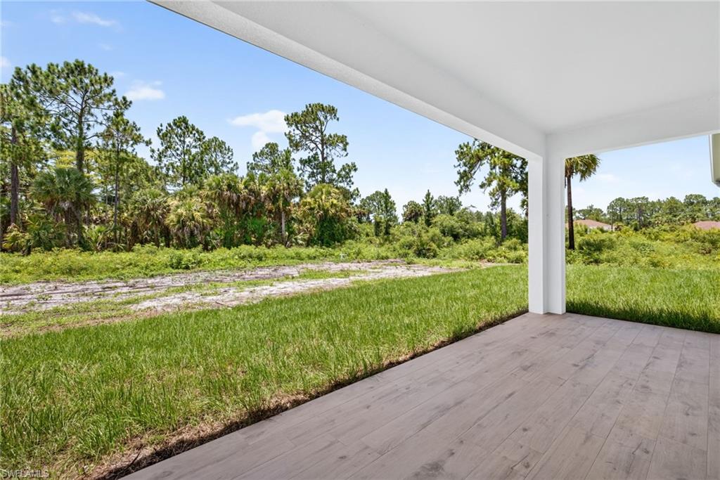Covered patio with wood-finish flooring, white columns, and a white ceiling, overlooking a lush green lawn and dense natural foliage