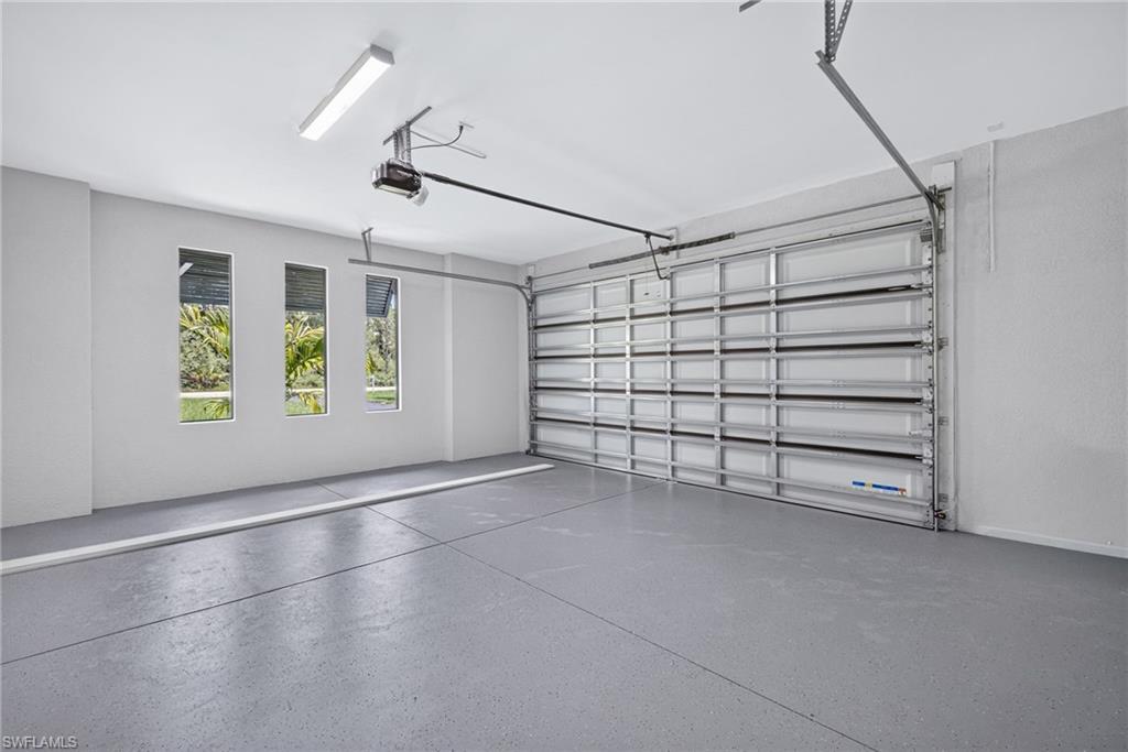 Spacious garage featuring a sectional garage door, automatic opener, three vertical windows, overhead fluorescent lighting, and a grey epoxy-coated concrete floor
