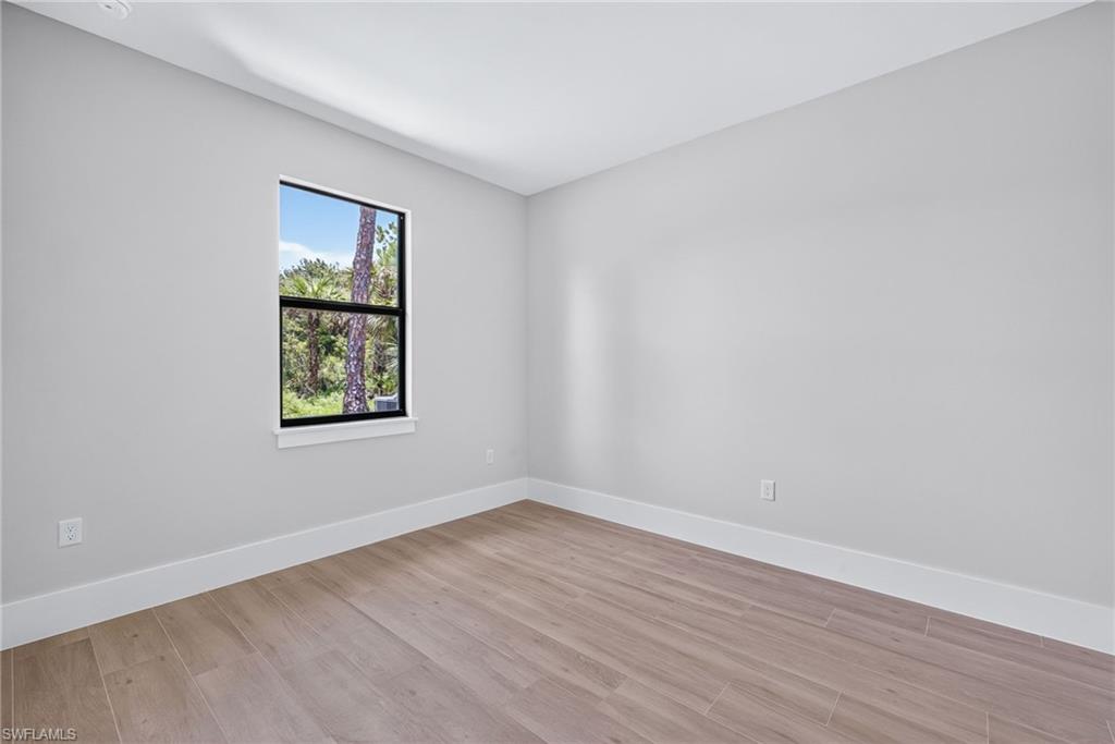 Light-filled room featuring wood-finish flooring, white baseboards, and a window with black trim