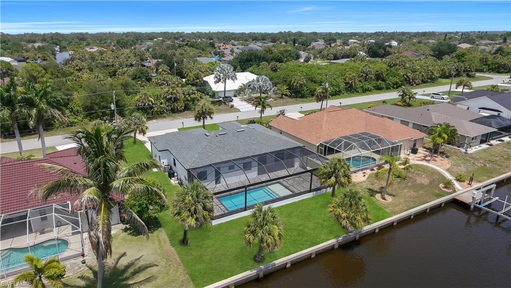 Waterfront property featuring a screened-in pool, lush green lawn, mature palm trees, and a private dock