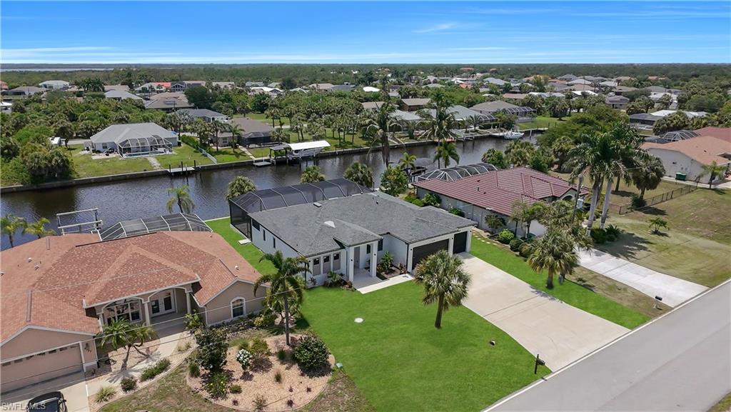 Waterfront property featuring a private boat dock, screened pool enclosure, paved driveway, and mature palm trees