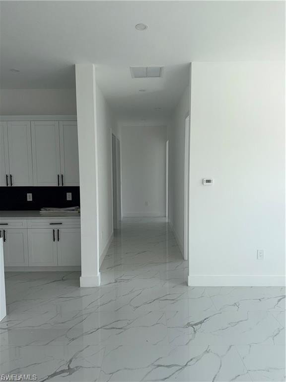 Spacious interior featuring pristine white walls, large format tile flooring with a subtle marble-like pattern, recessed lighting, and white cabinetry with black hardware