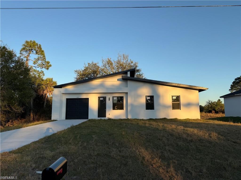 Modern architecture featuring a white stucco exterior, black windows, a black entry door, a black garage door, and a concrete driveway