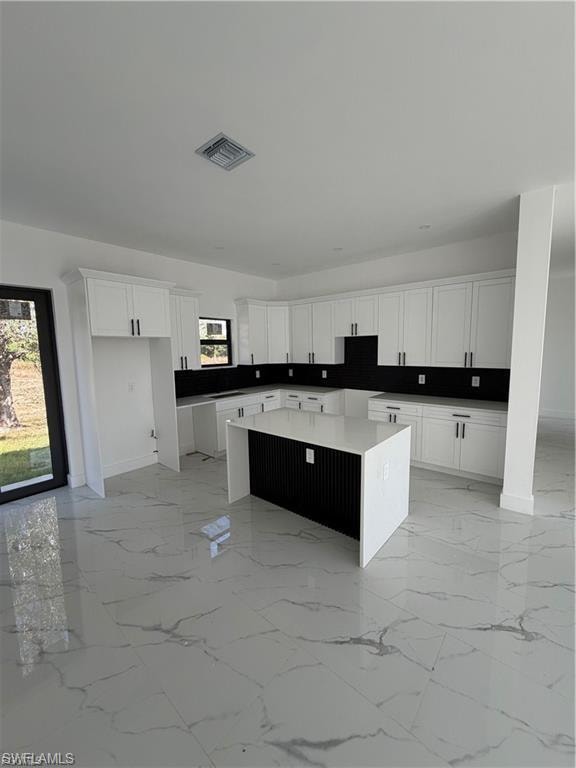 Kitchen featuring white cabinetry with dark hardware, dark countertops, a large center island with a white waterfall edge countertop, and large format white tile flooring with grey veining