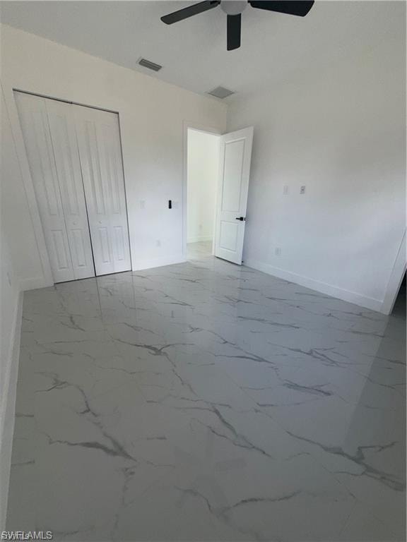 Spacious interior room featuring large format tile flooring with a marble-effect pattern, white walls, and a ceiling fan