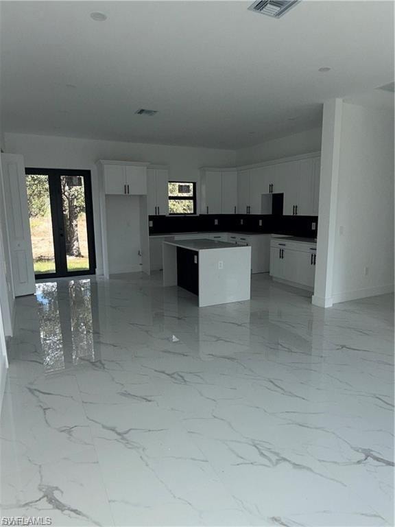 Open-concept kitchen and living area featuring marble-look tile flooring, white shaker cabinetry, a two-tone kitchen island, and a black glass-paneled double door
