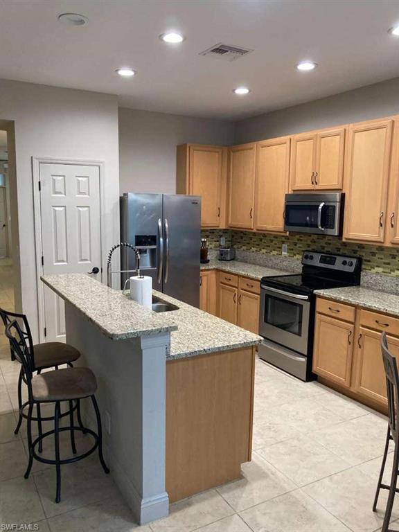 Kitchen featuring light wood-finish cabinetry, granite-style countertops, stainless steel appliances, and recessed lighting