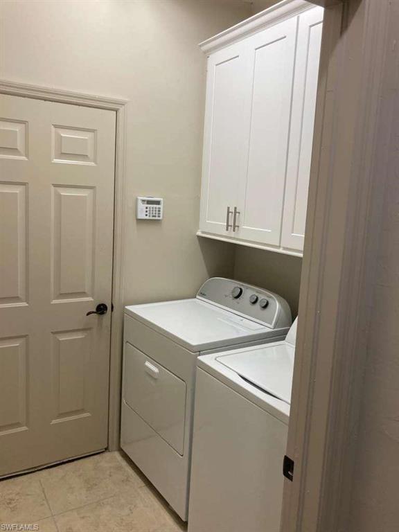 Laundry area with overhead white cabinetry, tile flooring, and a paneled door with dark hardware