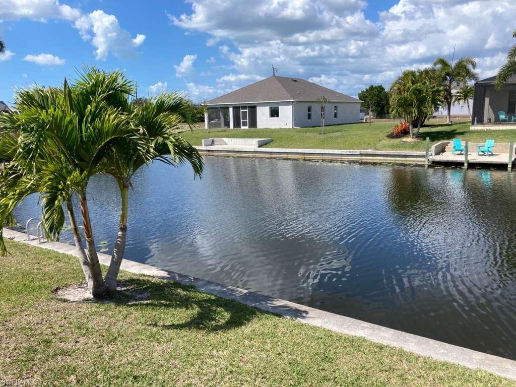 Waterfront property featuring a stucco exterior with a screened porch, a flat-bottom canal, and mature landscaping