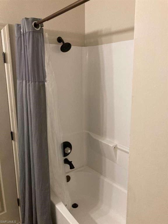 White acrylic tub and shower combination with dark bronze fixtures and a built-in grab bar
