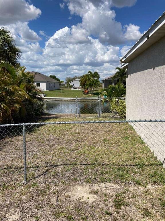 Canal-front property featuring a chain-link fence, a private gate to the canal, and mature tropical landscaping
