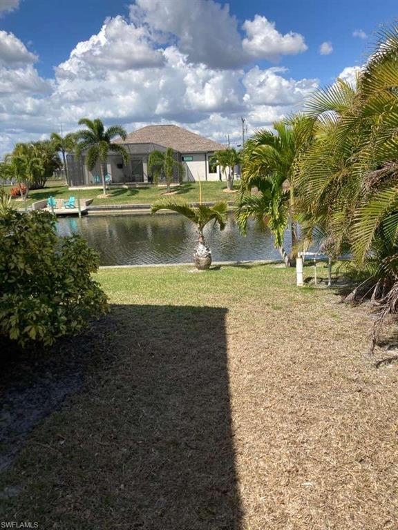 Waterfront property featuring a canal, a dock with two chairs, and a small palm tree