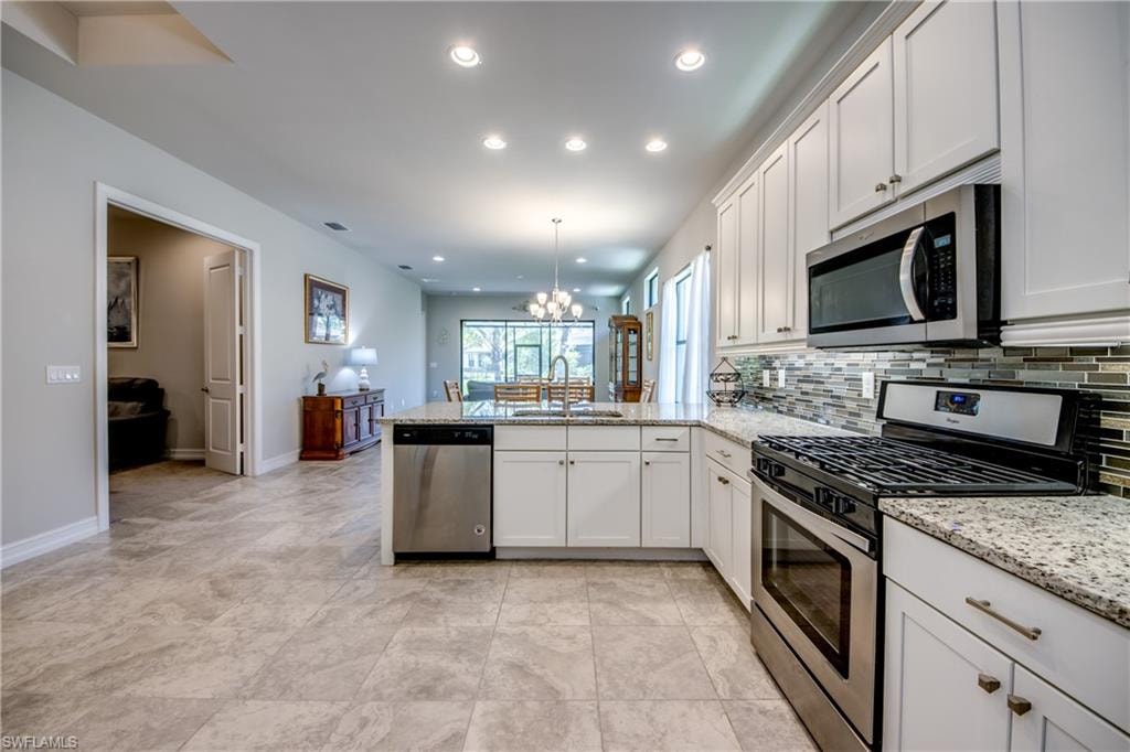 Modern kitchen featuring white shaker cabinetry, stainless steel appliances, speckled stone countertops, and a glass tile backsplash