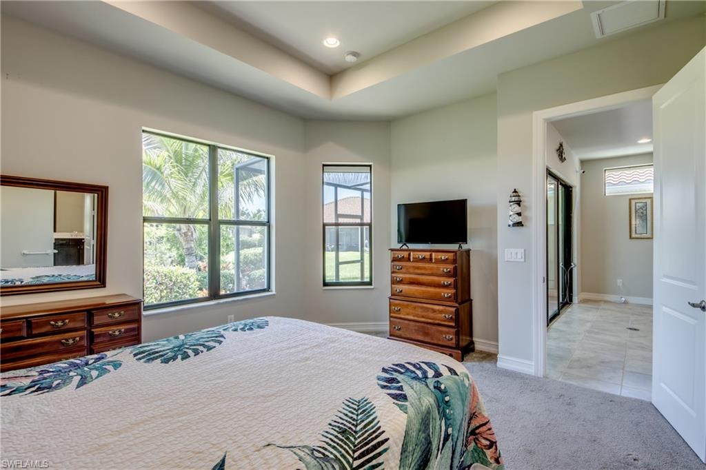 Recessed lighting and a tray ceiling accent this carpeted room, featuring multiple windows with outdoor landscaping visible