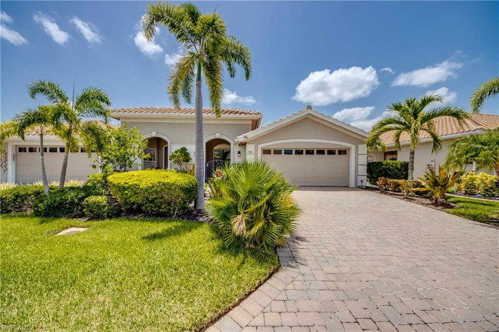 Property exterior featuring a paver driveway, lush green lawn, mature palm trees, and manicured shrubbery