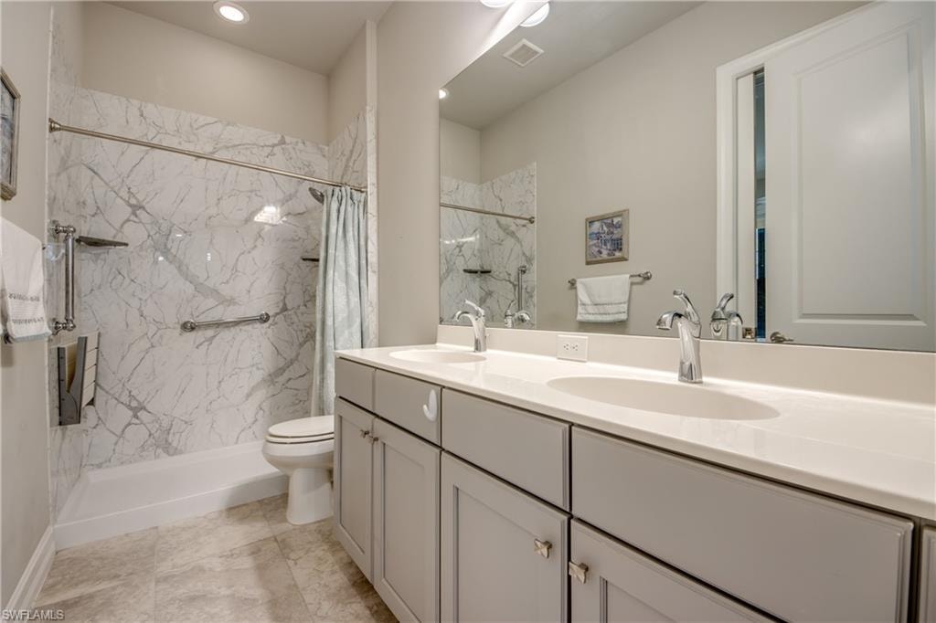 Bathroom featuring a dual vanity with light gray cabinetry, chrome hardware, and white countertops