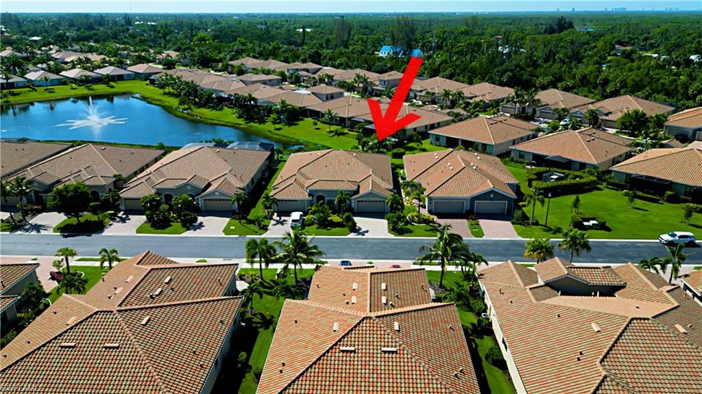 Aerial perspective highlighting a residential community with tile-roofed homes, mature landscaping, and a central pond featuring a fountain