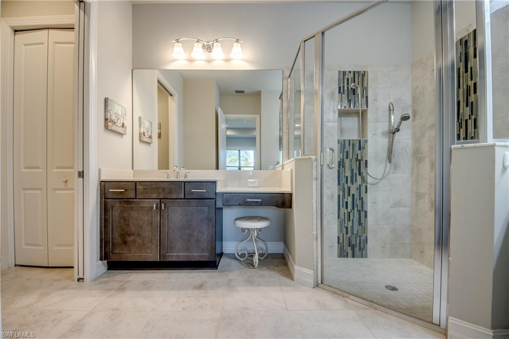 Bathroom featuring a glass-enclosed shower with decorative tile accents, dark wood-finish vanity with countertop, large mirror, and dual bi-fold closet doors