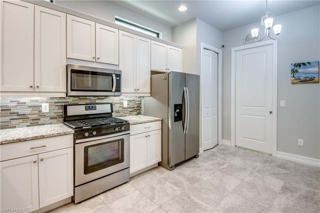 Kitchen featuring stainless steel appliances, speckled countertops, subway tile backsplash, white cabinetry, and large format floor tiling