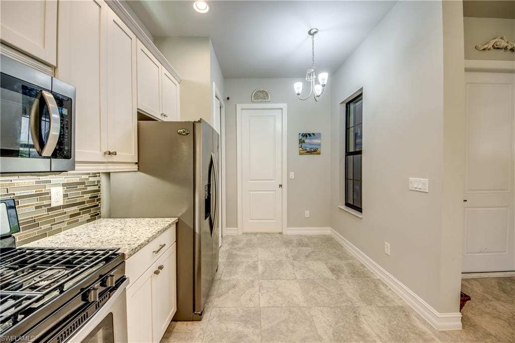 Galley kitchen featuring white cabinetry, stainless steel appliances, a multi-tone tile backsplash, and light-toned countertop