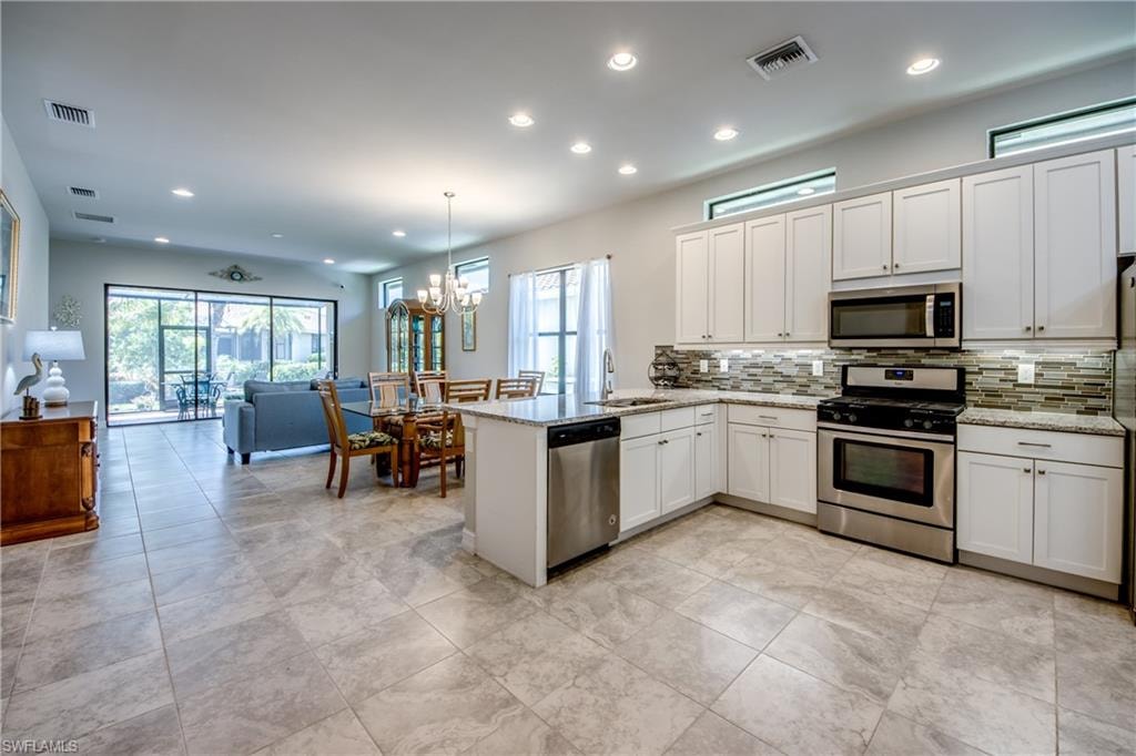 Open-concept living space featuring a contemporary kitchen with white cabinetry, stainless steel appliances, and a mosaic tile backsplash