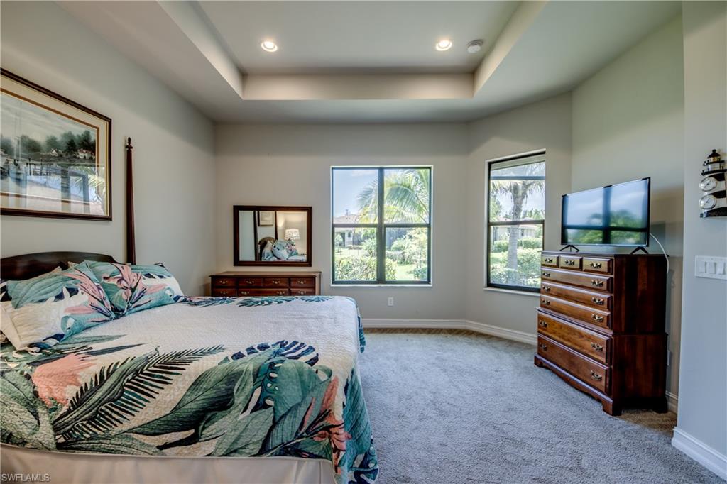 Spacious bedroom featuring a tray ceiling with recessed lighting, two large windows, and neutral carpeting