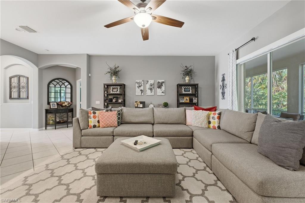Spacious living area featuring light gray wall paint, tiled flooring, an arched doorway, and large sliding glass doors providing abundant natural light