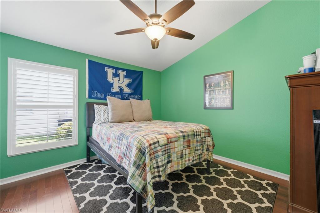 Room featuring a vaulted ceiling with a ceiling fan light fixture, wood-finish flooring, and a window with white louvered shutters