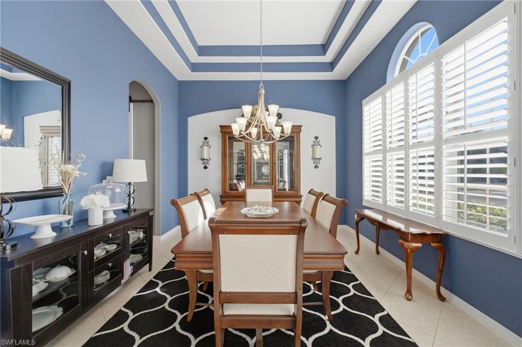 Formal dining area featuring a tray ceiling, arched doorway, and ceramic tile flooring