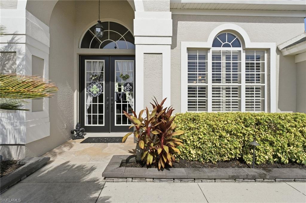 Stucco exterior with arched entry, double glass-paneled front doors, transom window, and plantation shutters