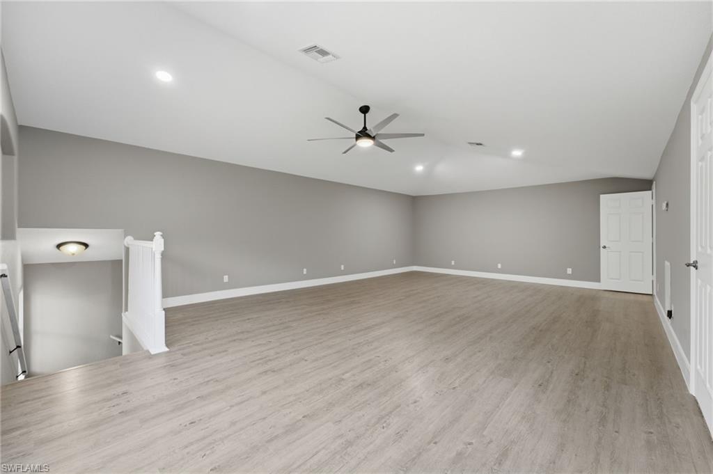 Spacious room featuring vaulted ceilings, recessed lighting, wood-finish flooring, a contemporary ceiling fan, and crisp white trim