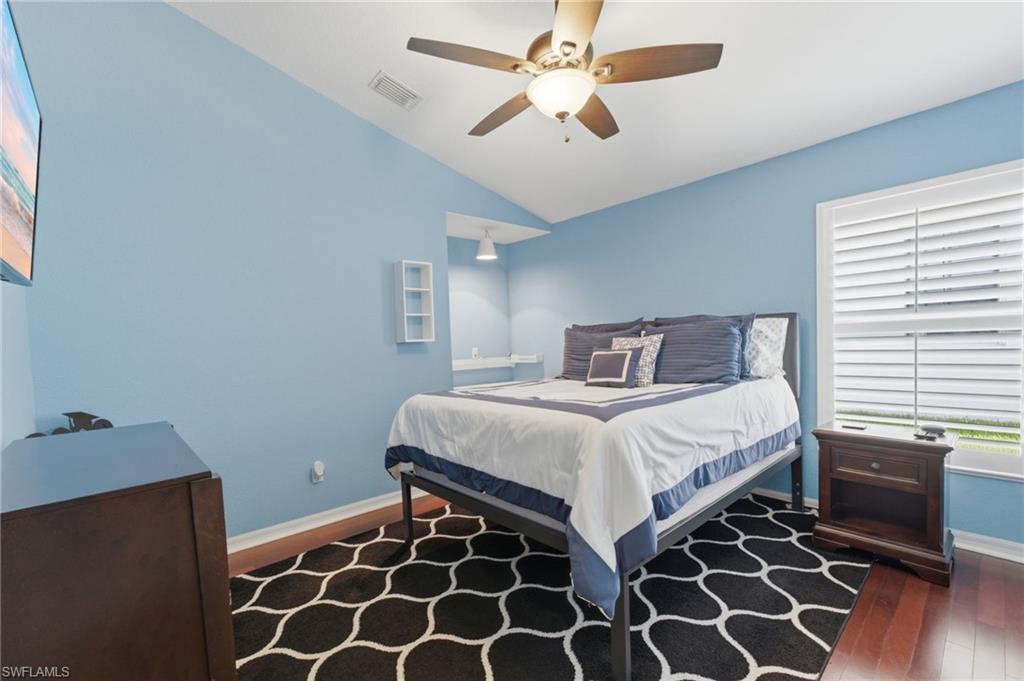 Spacious room featuring vaulted ceilings, a ceiling fan with integrated lighting, a built-in recessed alcove with shelf, a large window with plantation shutters, and wood-finish flooring