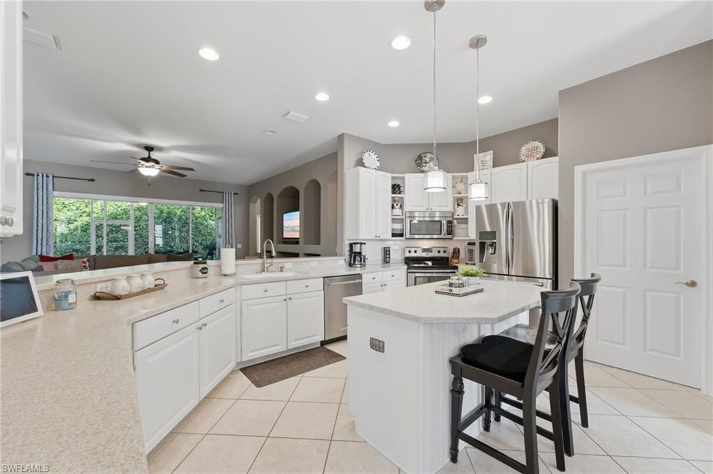 Kitchen featuring white cabinetry, light-toned countertops, a central island with pendant lighting, stainless steel appliances, and tile flooring