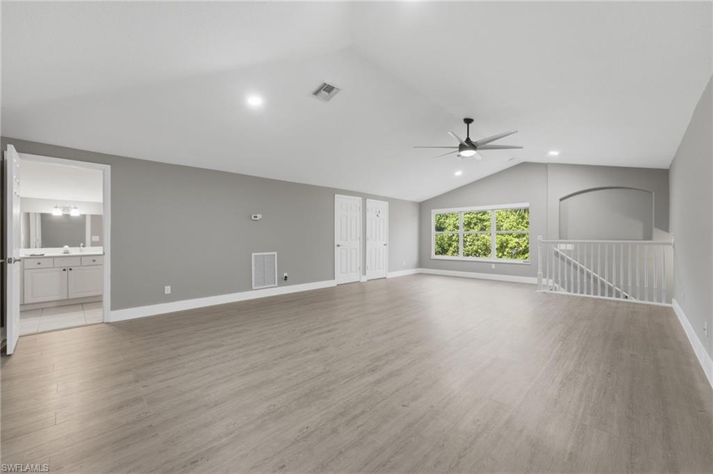 Spacious room featuring vaulted ceilings, recessed lighting, wood-finish flooring, a contemporary ceiling fan, and large windows with exterior foliage