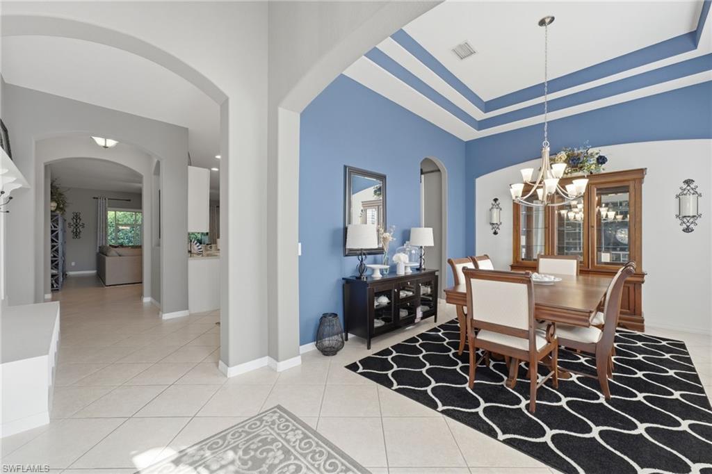 Dining area with tray ceiling featuring accent paint, tile flooring, and arched doorways