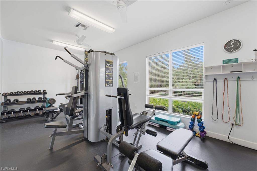 Dedicated fitness space featuring rubber flooring, abundant natural light from large windows, two ceiling fans, and overhead fluorescent lighting