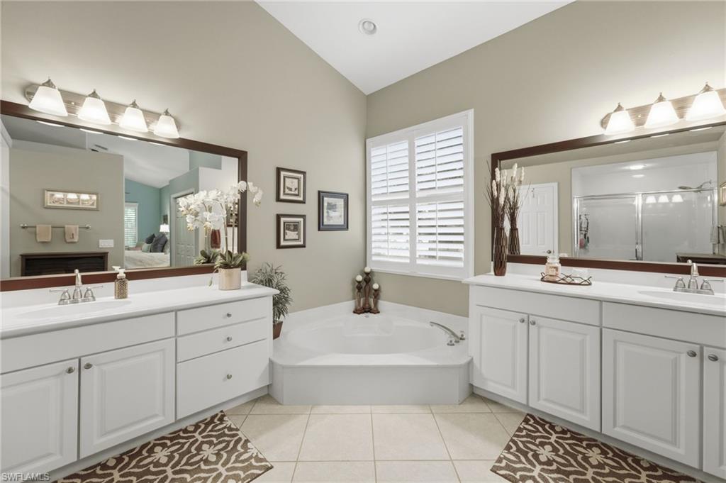 Spacious bathroom featuring a built-in corner soaking tub, dual vanities with white cabinetry, large framed mirrors, and plantation shutters