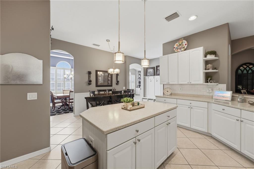 Kitchen featuring an island, white cabinetry, light countertops, subway tile backsplash, and tile flooring
