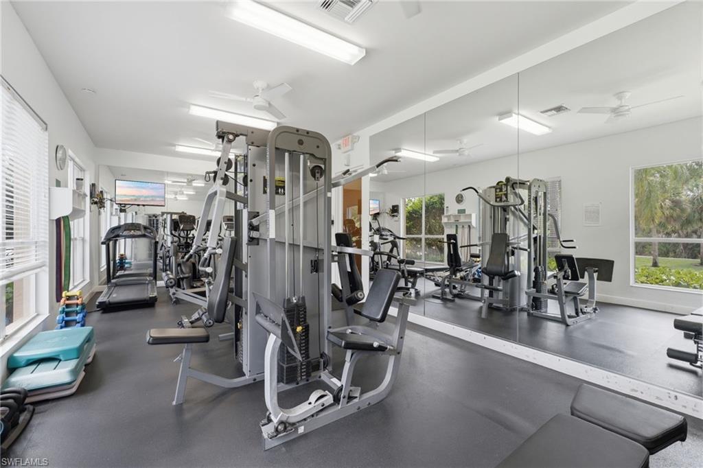 Spacious fitness room featuring a full wall of mirrors, multiple exercise machines, rubber flooring, and ample natural light from several windows
