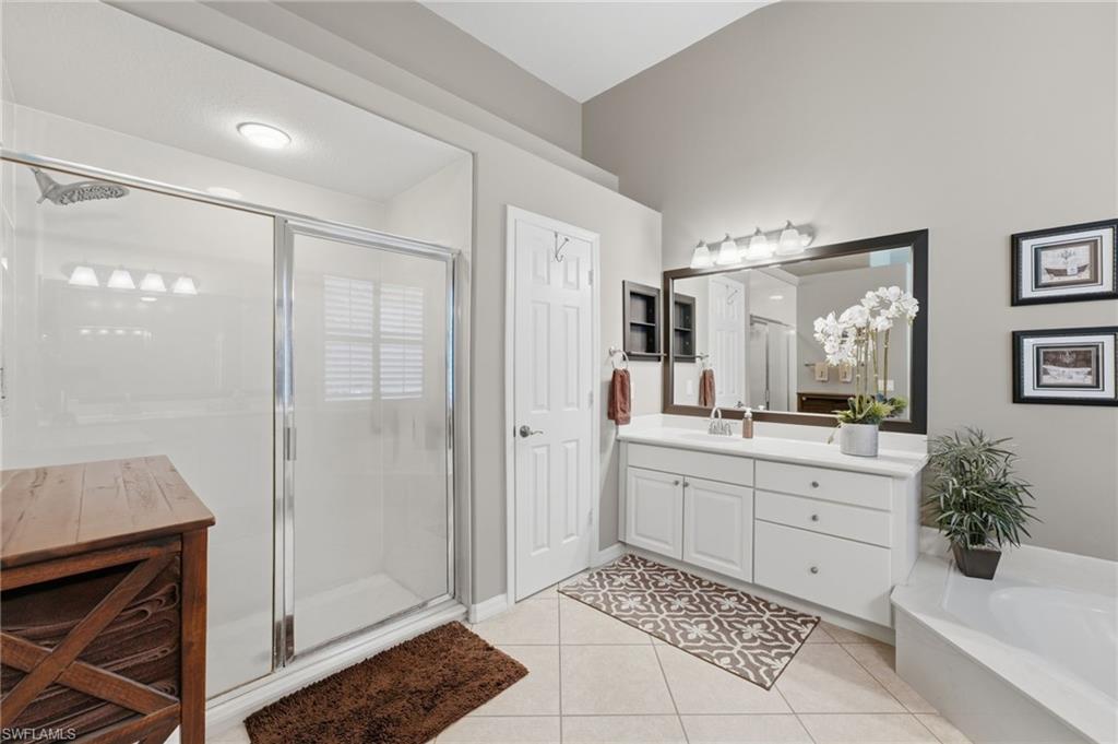 Bright bathroom featuring a large glass-enclosed shower, a white vanity with extensive counter space, an integrated drop-in soaking tub, and a spacious framed mirror with overhead lighting