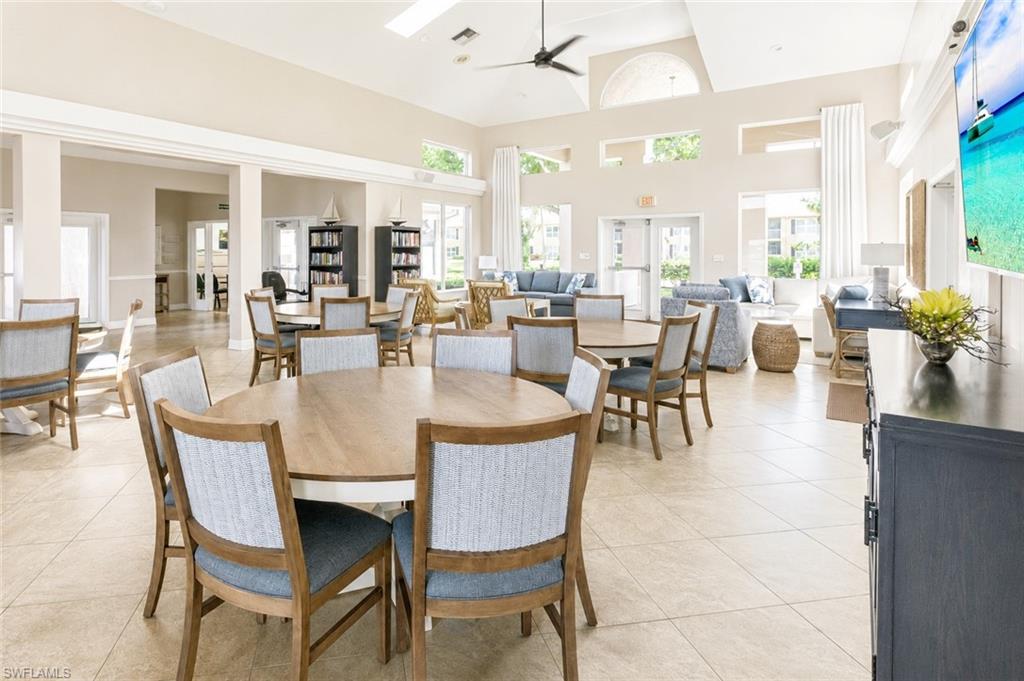 Spacious common area featuring light-toned tile flooring, high vaulted ceilings with a ceiling fan, and multiple large windows for ambient light