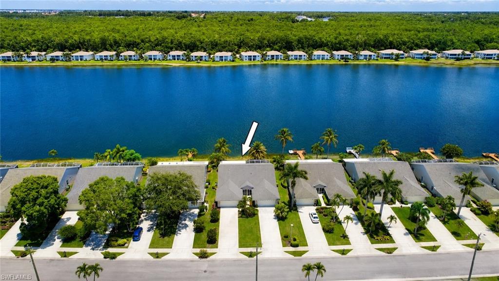 Waterfront property featuring a private dock, mature palm trees, manicured landscaping, and a driveway with an attached garage