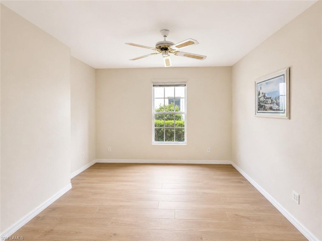 Spacious room featuring light-toned walls, wood-finish flooring, a ceiling fan, and a double-hung window