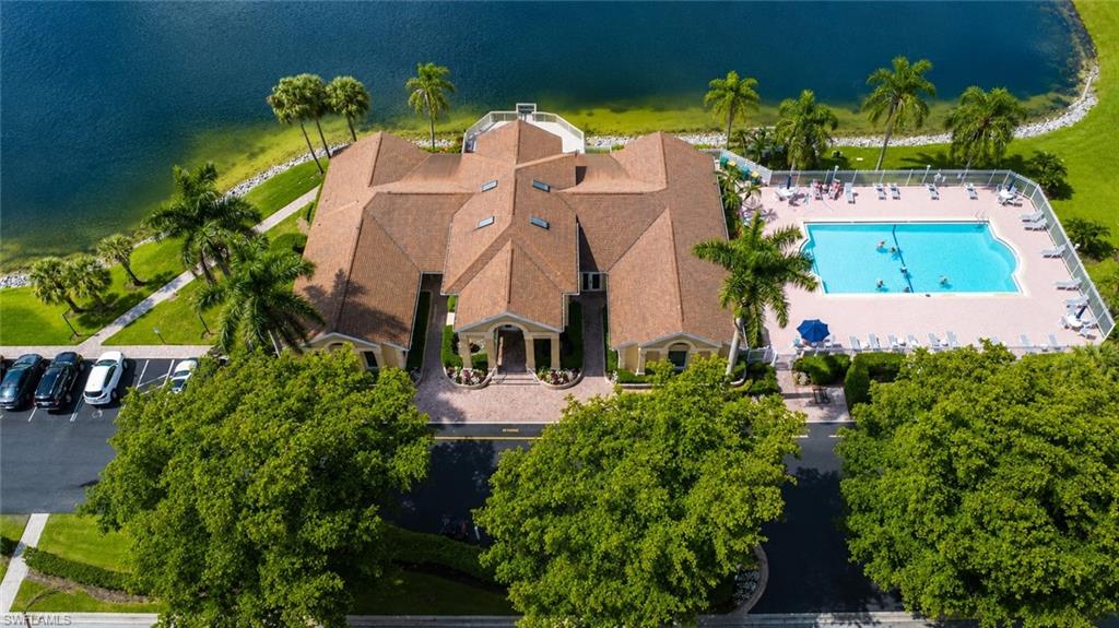 Community clubhouse building featuring a terracotta tile roof, a swimming pool with surrounding lounge chairs, and a paved parking area